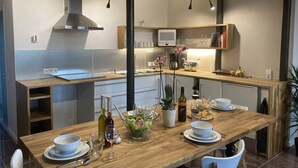 A modern kitchen with a wooden dining table set for a meal, a built-in oven, and a clock on the wall. - Ferienidylle Haus Königsberg, Child-friendly, Dog-friendly, Barrier-free (Michelstadt)