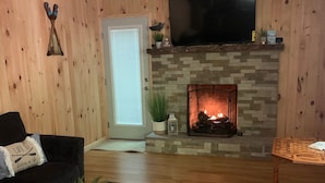 A living room with a stone fireplace, a television mounted above it, and a wooden wall. - Welcome to Mountain Momma (Mount nebo)