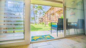 A hotel entrance with a sliding glass door leading to a balcony with a view of palm trees and a building with multiple balconies.