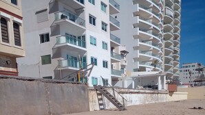 Une plage avec un chien, un mur en béton et un immeuble à plusieurs étages doté de balcons.