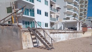 Une plage de sable avec un escalier menant à un bâtiment doté de plusieurs balcons.