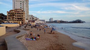 Une plage avec une promenade sinueuse, des gens qui se détendent et des bâtiments en arrière-plan.