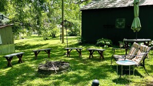 A grassy outdoor area with picnic tables, a fire pit, a hammock, and a small shed.