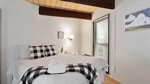 Un dormitorio con cama, mesita de noche, lámpara, ventana con persianas y un cuadro colgado en la pared.
