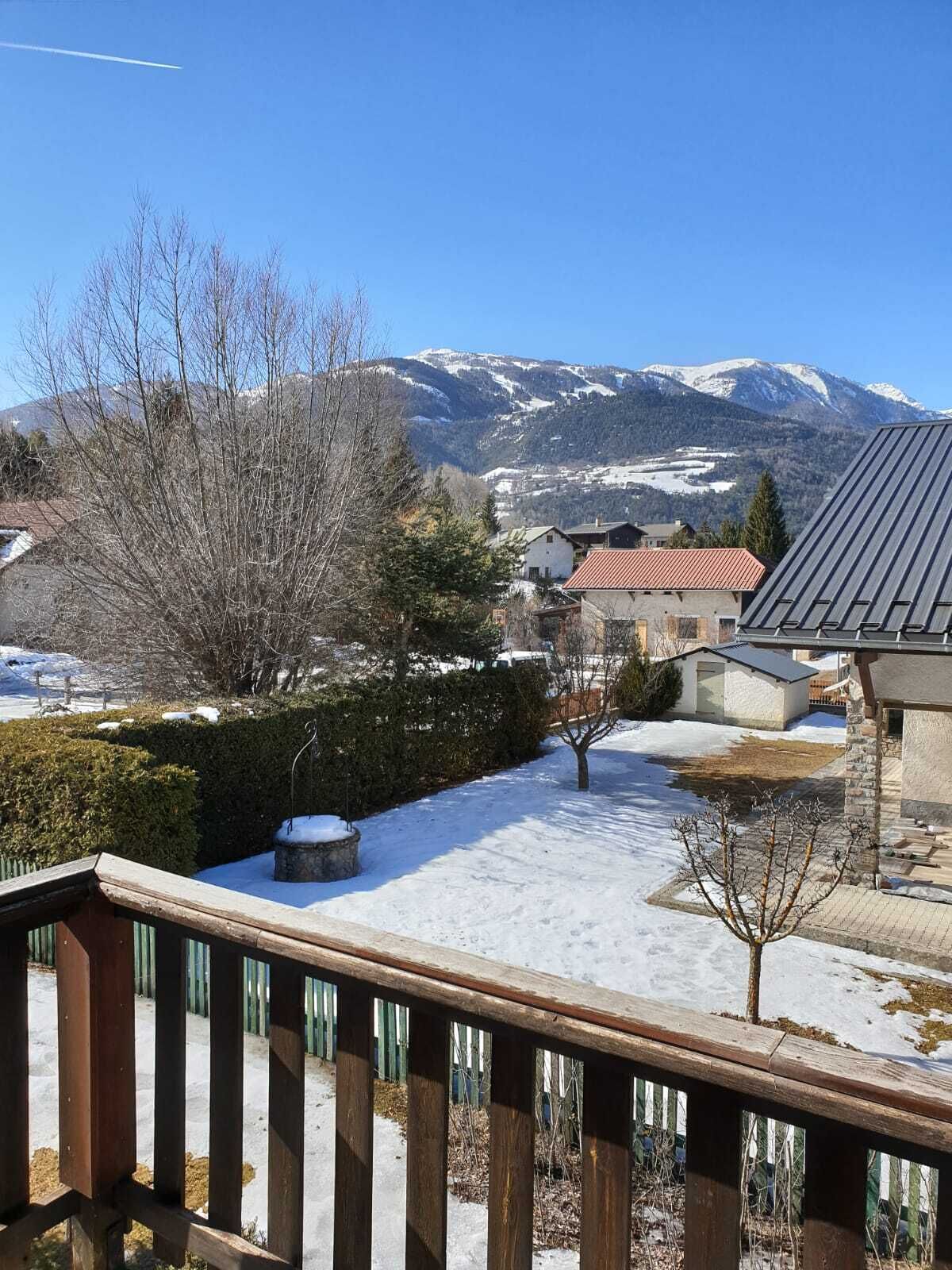 A snowy landscape with a mountain in the background, a wooden deck, and a building with a red roof.