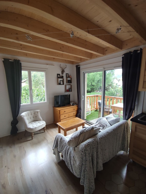 A cozy room with a wooden ceiling, a bed, a TV, a dresser, and a window overlooking a deck.