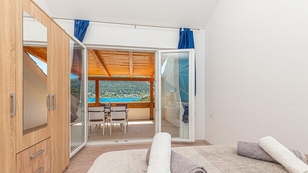 Una camera da letto con un armadio in legno, un letto con asciugamani arrotolati e un balcone con tavolo e sedie che offre una vista panoramica.