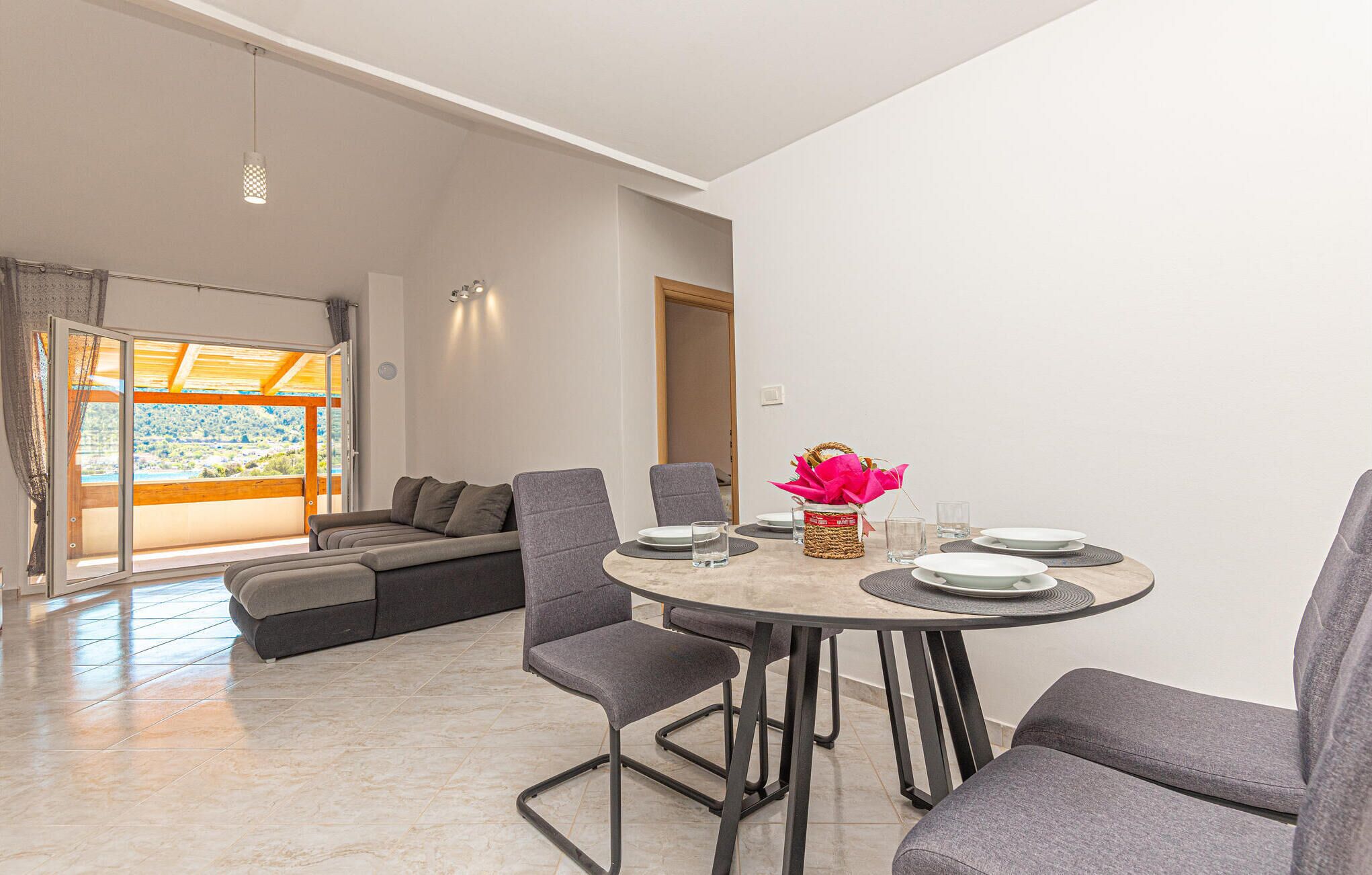 A modern dining area with a round table, grey upholstered chairs, and a vase with a pink flower arrangement.