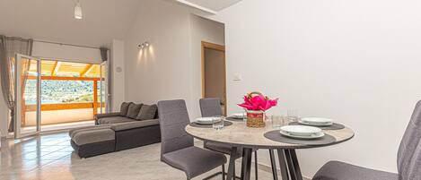 A modern dining area with a round table, grey upholstered chairs, and a vase with a pink flower arrangement.