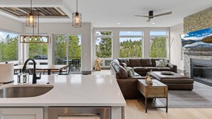 A modern kitchen with a large island, a dining area with outdoor seating, a cozy living room with a fireplace, and large windows offering a view of trees. - Luxury|Views|Hot Tub|Free Bus Route (Breckenridge)