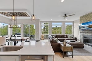 A modern kitchen with a large island, a dining area with outdoor seating, a cozy living room with a fireplace, and large windows offering a view of trees. - Luxury|Views|Hot Tub|Free Bus Route (Breckenridge)