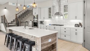 A modern kitchen with white cabinetry, a central island with stools, a built-in oven, microwave, and a stainless steel range hood. - Luxury|Views|Hot Tub|Free Bus Route (Breckenridge)