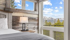 A bedroom with a bed, a nightstand, a lamp, and a view of mountains through a window. - Luxury|Views|Hot Tub|Free Bus Route (Breckenridge)