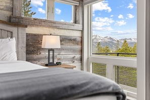 A bedroom with a bed, a nightstand, a lamp, and a view of mountains through a window. - Luxury|Views|Hot Tub|Free Bus Route (Breckenridge)