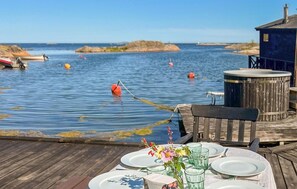 Terraza de madera con una mesa lista para comer, con vista a agua tranquila, boyas y barcos.