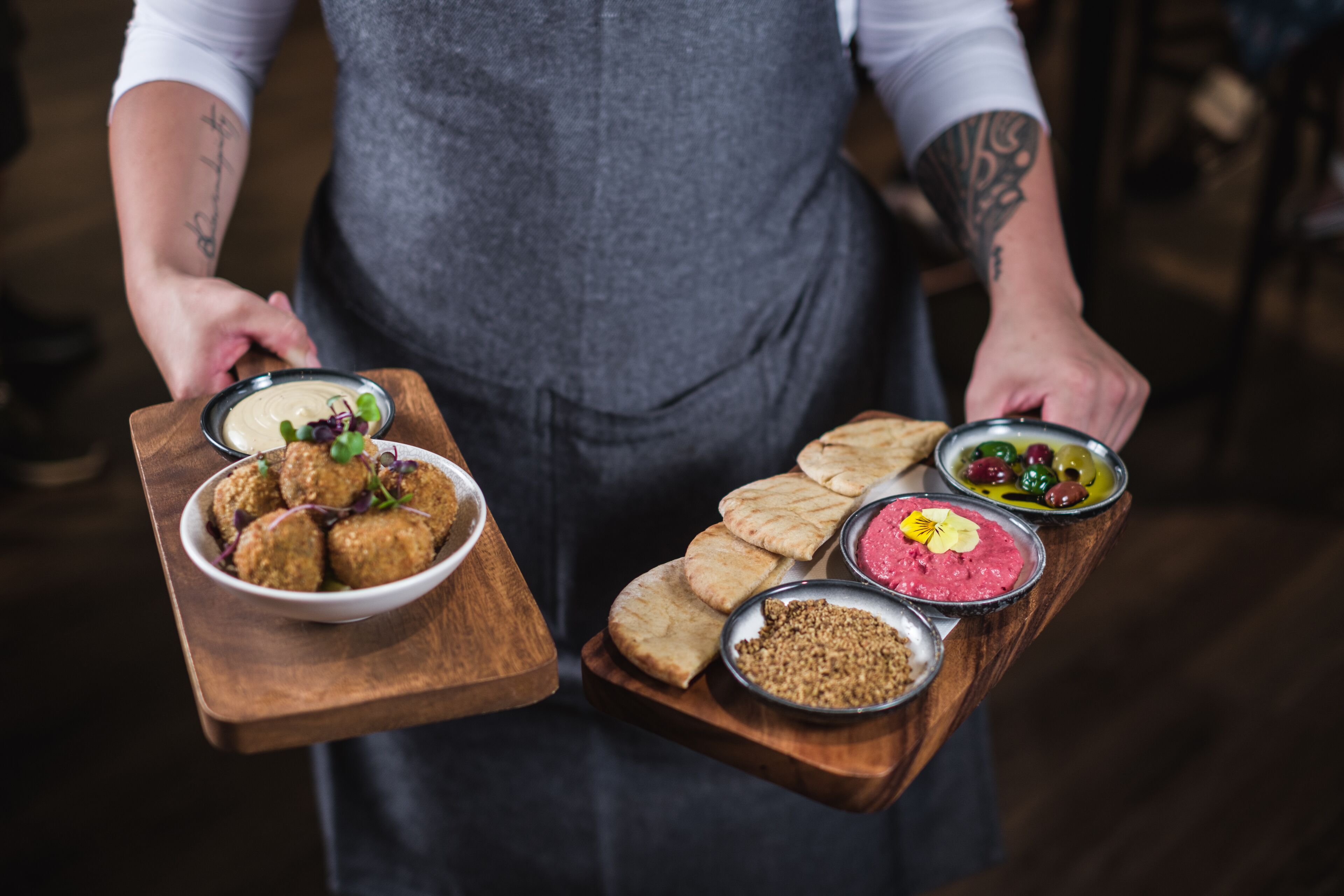 A person holding a wooden board with various food items including falafel, flatbreads, and dips.