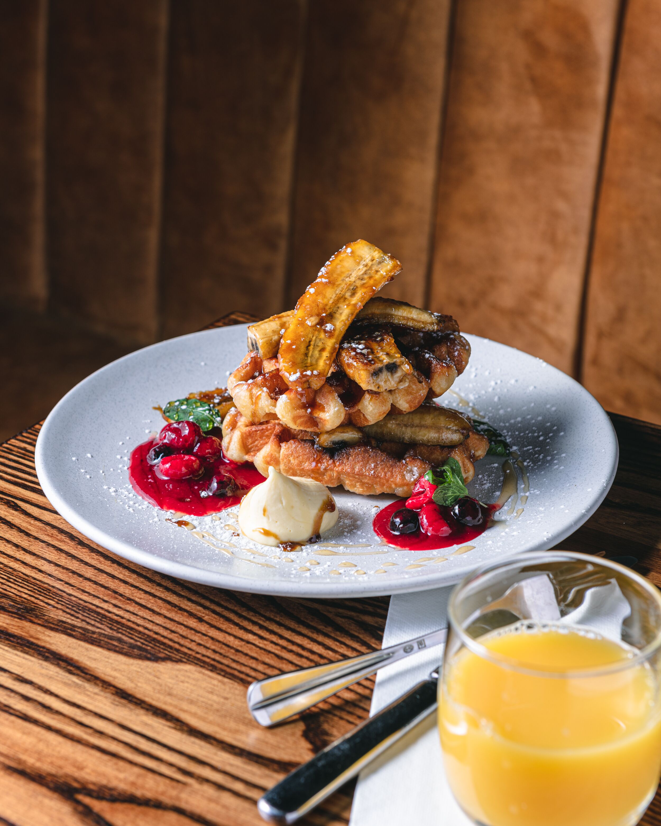 A plate of food with pancakes, a banana, berries, and a glass of orange juice on a wooden table.