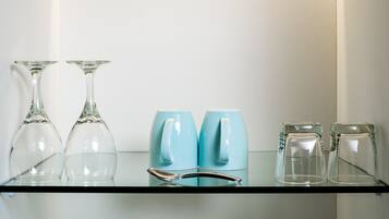 Une étagère en verre sur laquelle sont disposés divers objets en verre, notamment deux verres à vin, deux tasses bleues et deux petits verres.