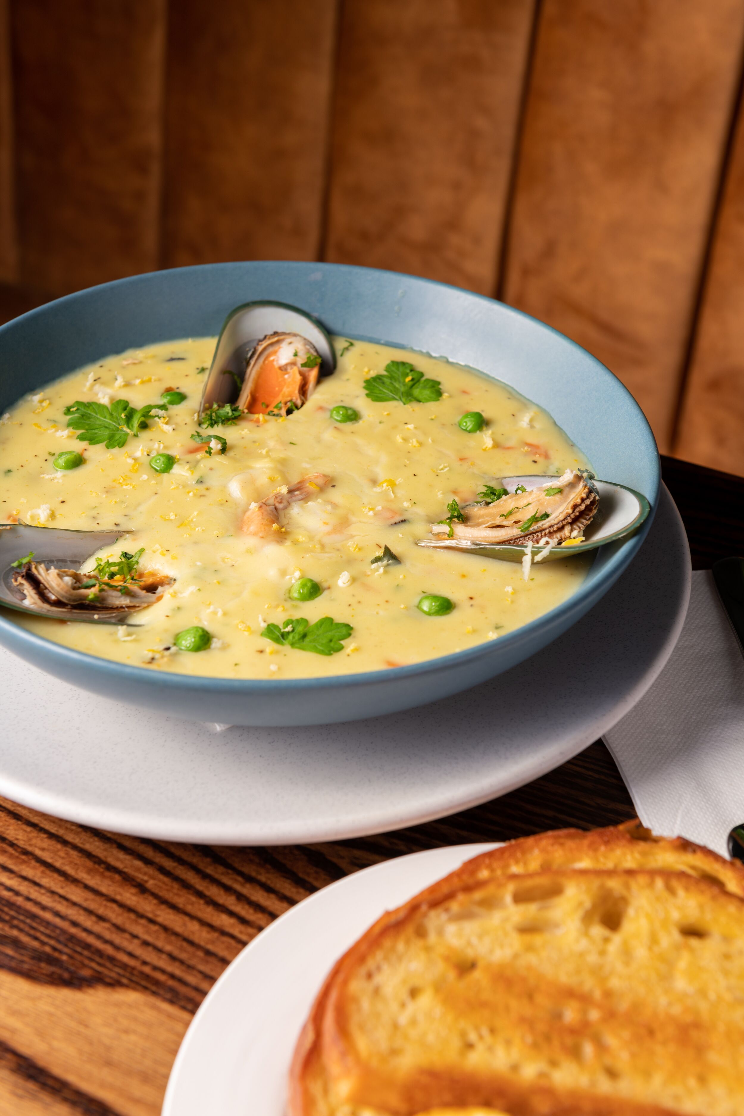 Una ciotola di zuppa di pesce con cozze e piselli, servita su un piatto blu con un cucchiaio.