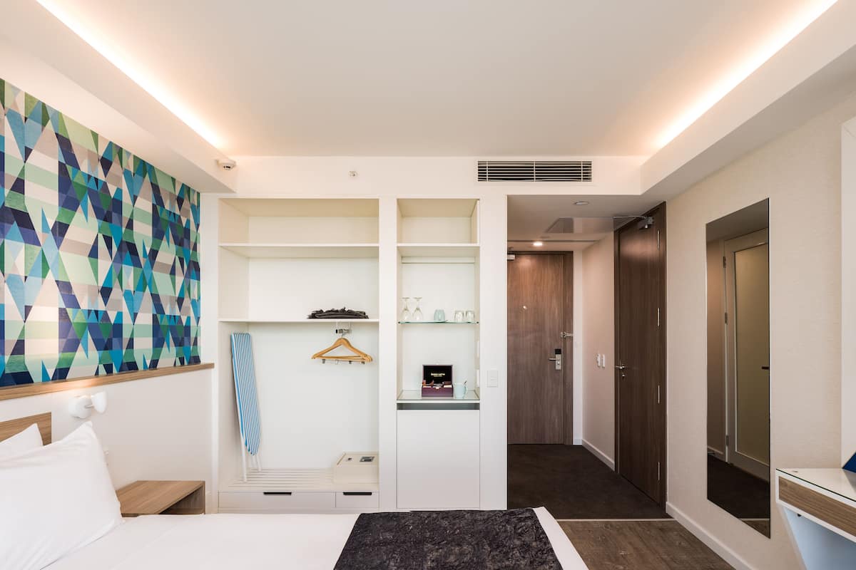 Ein modernes Hotelzimmer mit einem Bett, einem Kleiderschrank, einem Spiegel und einer Wand mit geometrischem Muster.
