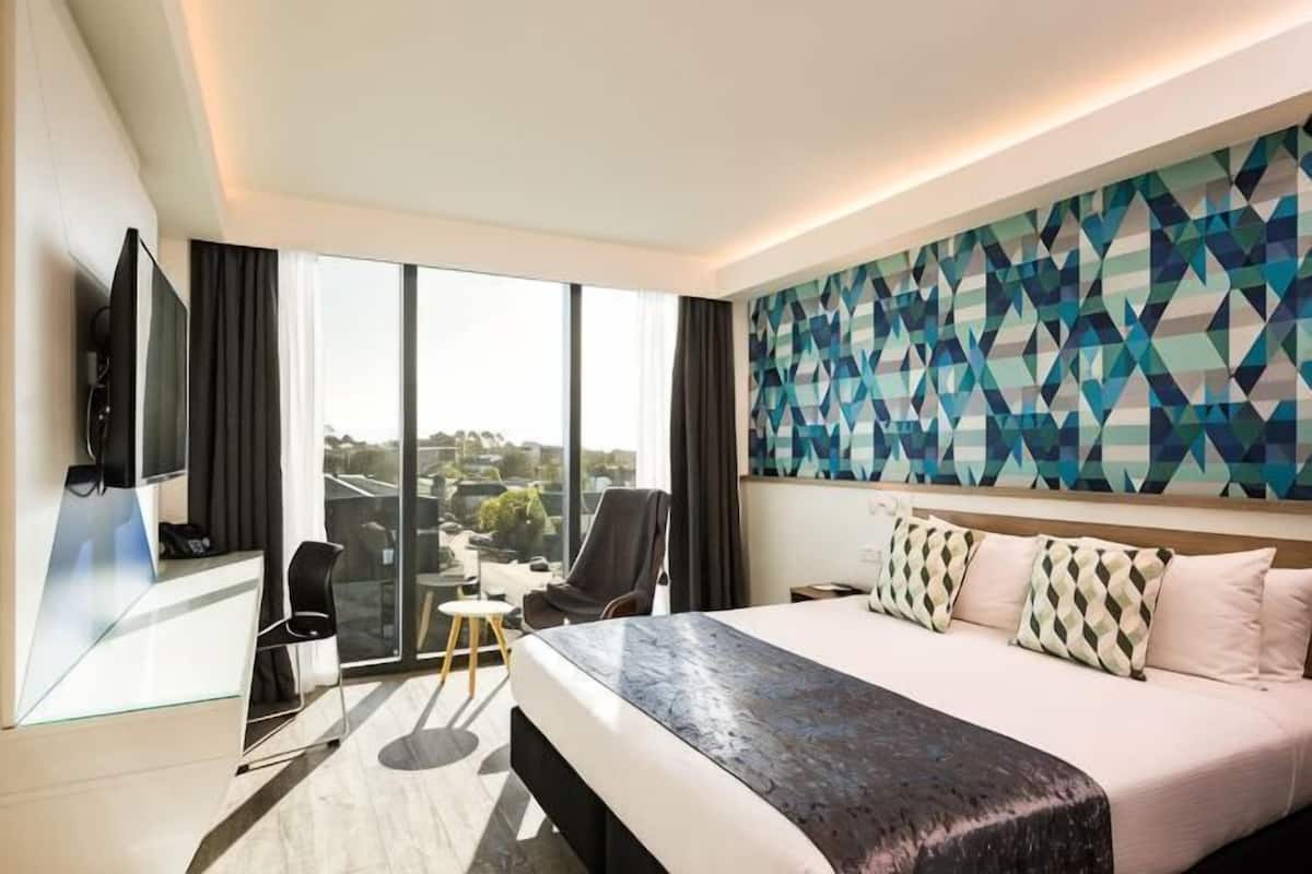 Ein Hotelzimmer mit einem großen Bett, einem Schreibtisch, einem Sessel, einem Fernseher und Blick auf die Stadt.