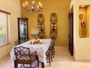 A dining area with a table set for six, surrounded by chairs, a chandelier, and wall-mounted candle holders.