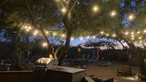 Un área de patio al aire libre con una parrilla, sillas de lounge y luces colgantes.