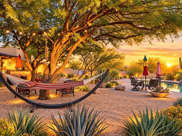 A hammock under a tree, outdoor seating, a pool, and desert plants.
