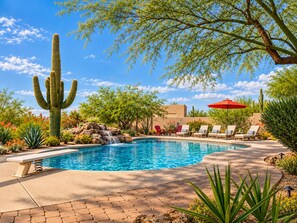 A pool with a waterfall feature, surrounded by desert plants and a large cactus.