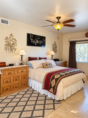 A bedroom with a bed, dresser, ceiling fan, artwork, and a window with curtains.