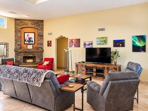 A modern living room with a stone fireplace, comfortable seating, a flat-screen TV, and various wall art.