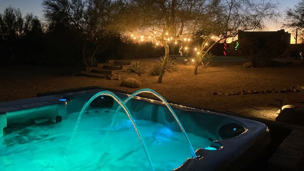 Una piscina al anochecer con fuentes y luces colgantes al fondo.