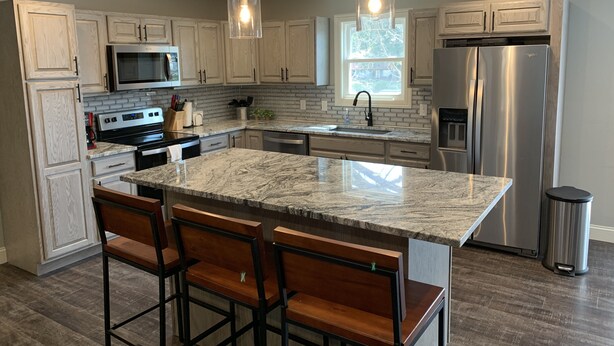 A modern kitchen with granite countertops, stainless steel appliances, and wooden bar stools. - Completely renovated home in Quiet Cove with a Dock! (Sunrise Beach)