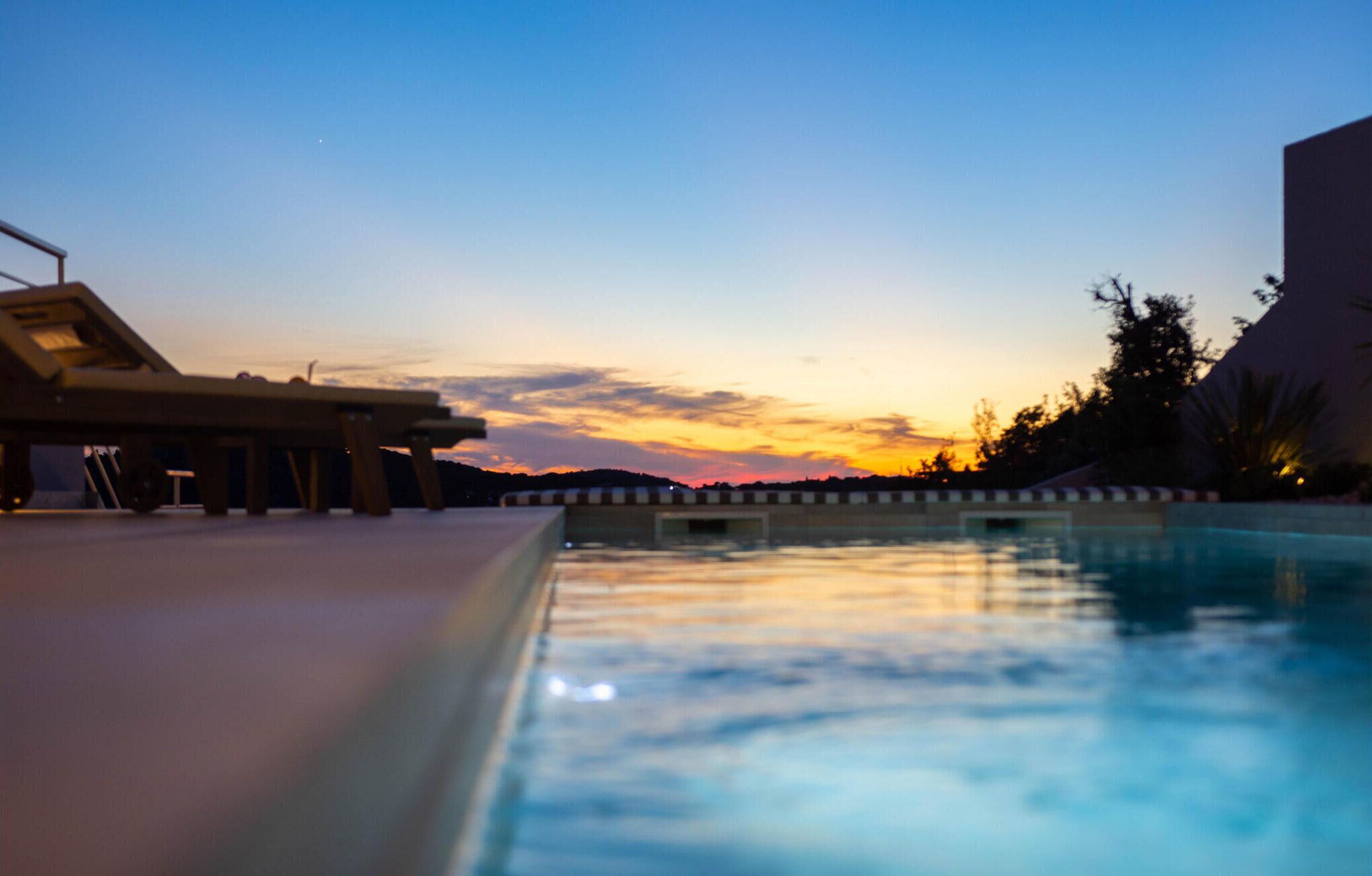 A swimming pool with a sunset view, lounge chairs, and a building in the background.