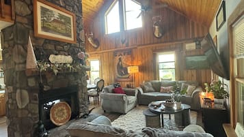 L’intérieur chaleureux d’un chalet avec une cheminée en pierre, un plafond en bois et un coin salon confortable.