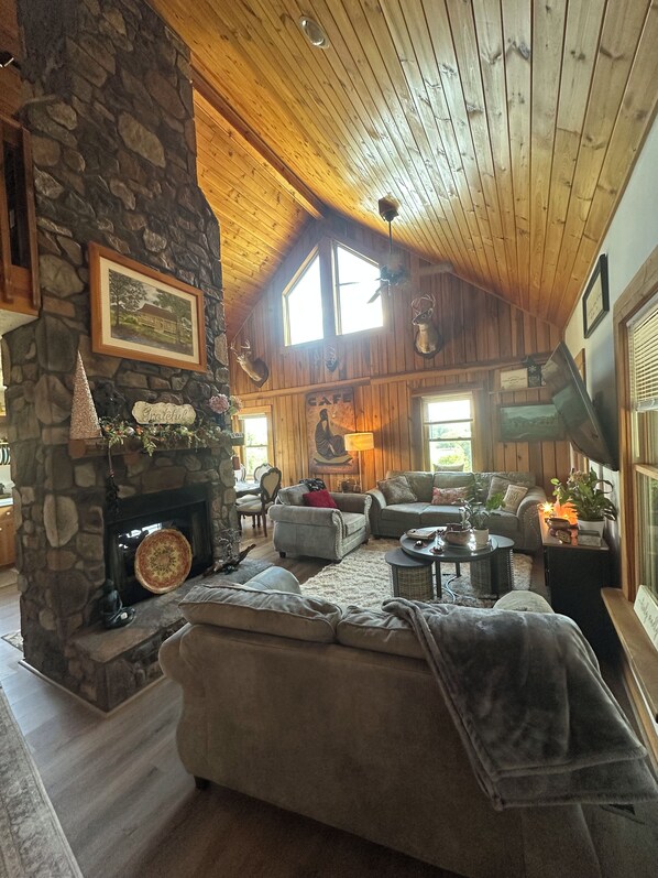 L’intérieur chaleureux d’un chalet avec une cheminée en pierre, un plafond en bois et un coin salon confortable.