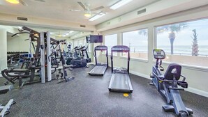 A gym with treadmills, weight machines, and a TV screen. - Large Luxury 2 Bedroom, 2 Bath Direct Ocean Front (Daytona Beach)