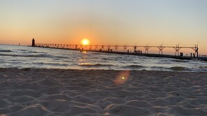 Una spiaggia con un molo che si protende nell'acqua, con un faro e persone che lo percorrono.