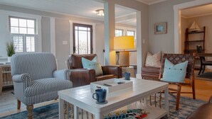 Un salon avec des fauteuils à rayures, un canapé en cuir marron, une table basse blanche et une tasse bleue.