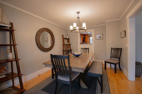 A dining area with a wooden table, chairs, a chandelier, and a mirror on the wall. - Beautifully Modern Downtown Ogunquit Home (Ogunquit)