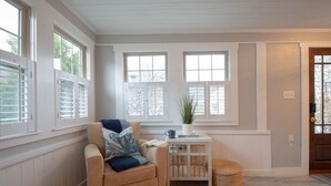 Une pièce avec un fauteuil beige, une petite table blanche ornée d’une plante et un tapis bleu.