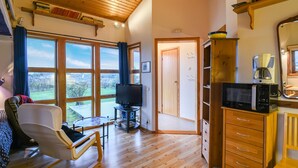 A cozy room with a wooden ceiling, large windows, a TV, a coffee maker, and a bookshelf. - 1 bedroom nice home in Bohus-Malmön (Bohus-Malmön)