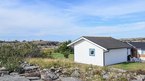 A small white building with a blue door and window, surrounded by rocks and vegetation, with a clear sky in the background. - 1 bedroom nice home in Bohus-Malmön (Bohus-Malmön)