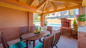 Une terrasse couverte avec une table et des chaises en bois, un mur en briques et un four en briques.