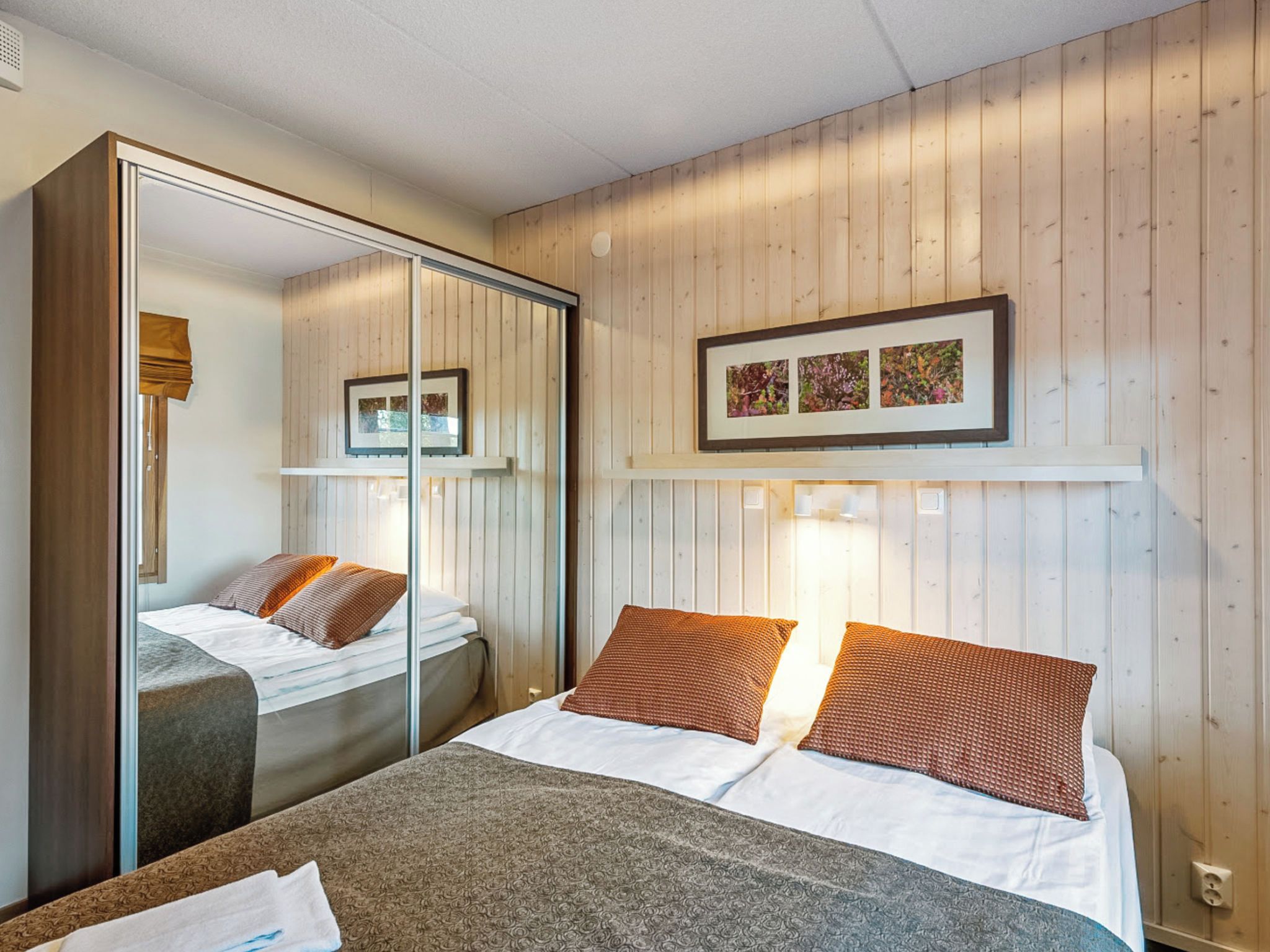 A hotel room with a bed, a mirror, a wardrobe, and a framed picture on the wall.