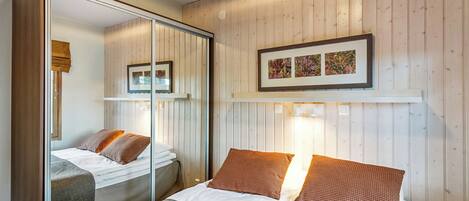 Ett hotellrum med en säng, en spegel, en garderob och en inramad tavla på väggen.