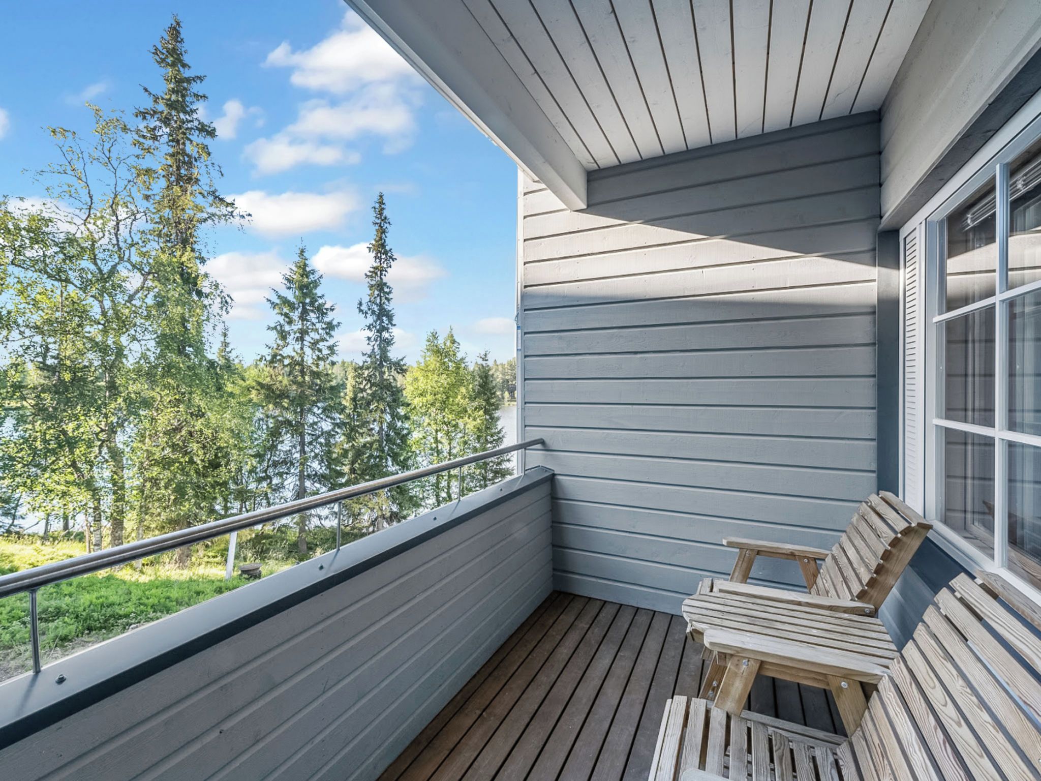 A balcony with a wooden deck, metal railing, and a view of trees and sky.