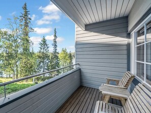 A balcony with a wooden deck, metal railing, and a view of trees and sky.