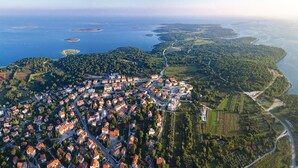 Vista aerea di una cittadina costiera con un fitto gruppo di case, una strada sinuosa e una costa punteggiata da diverse piccole isole.