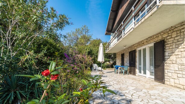 Un patio con pavimentazione in pietra, arredi da esterno, un edificio in pietra con persiane e vegetazione rigogliosa.